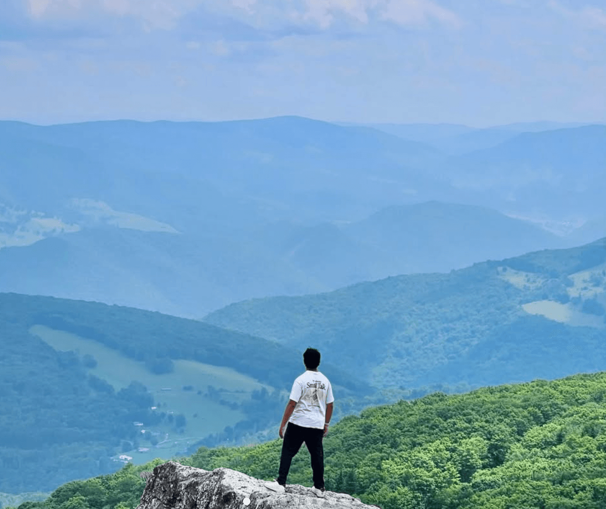 Ritviik standing on a rock overlook above green mountains